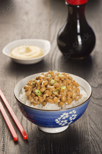 Bowl of Natto (Japanese Fermented Soybeans) on Rice with Soy Sauce and Mustard in Background