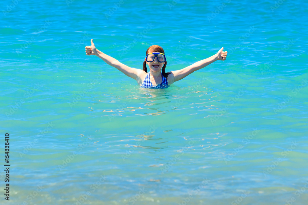 Happy girl in diving mask shows thumbs up standing in sea or ocean. Happy summer concept