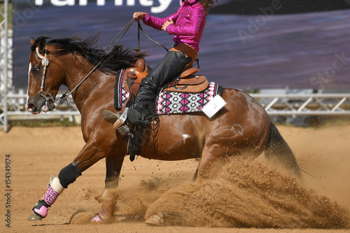 The side view of a rider in cowboy chaps and boots sliding the horse in the sand