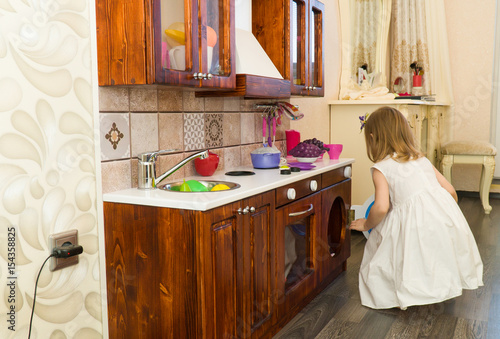 Active little preschool age child, cute toddler girl with blonde curly hair, shows playing kitchen, made of wood, plays in the kitchen photo