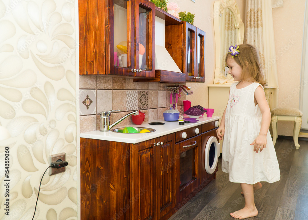 Active little preschool age child, cute toddler girl with blonde curly hair, shows playing kitchen, made of wood, plays in the kitchen Active little preschool age child, cute toddler girl with blonde curly hair, shows playing kitchen, made of wood, plays in the kitchen