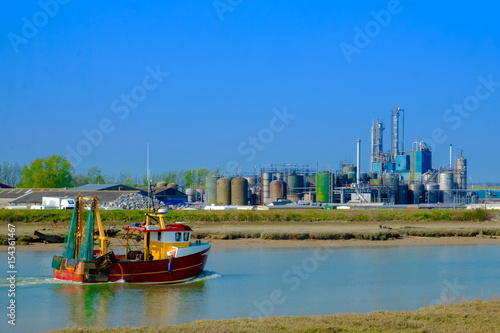 Fishing boat passing a oil and gas company on the river Rother  near Rye, East Sussex England