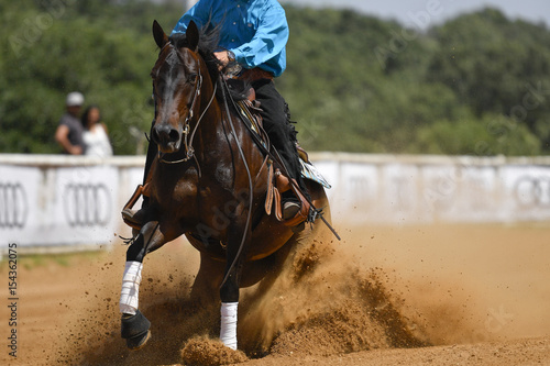 The frontview of a rider in cowboy chaps and boots sliding the horse in the sand