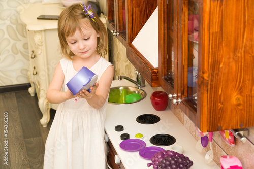 Active little preschool age child, cute toddler girl with blonde curly hair, shows playing kitchen, made of wood, plays in the kitchen photo