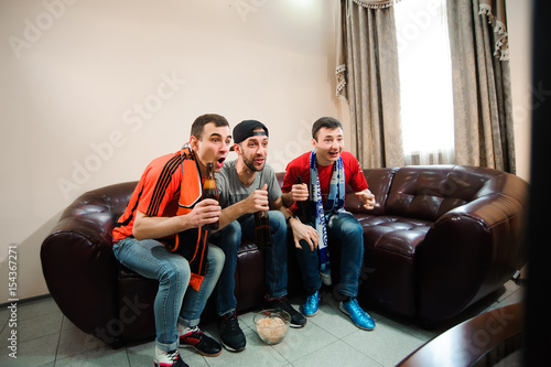 Young men drink beer, eat chips and root for football