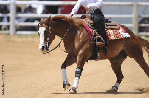 The side view of a rider in cowboy chaps and boots riding a horse 