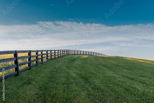 Black Fence Leads Over Grassy Hill