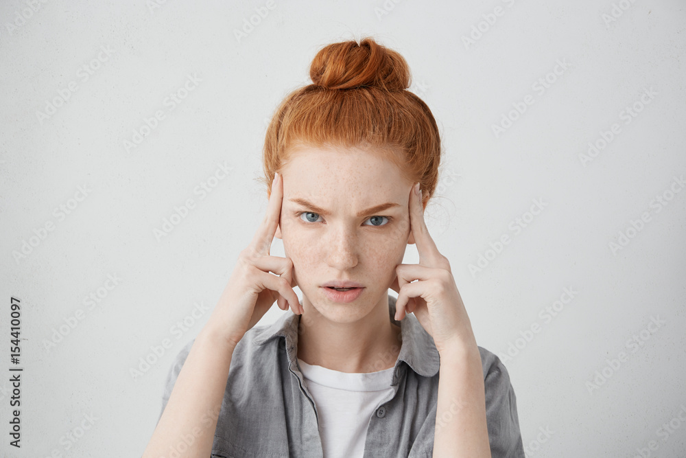 Close up shot of stressed unhappy young Caucasian woman wearing her ginger hair in bun, keeping