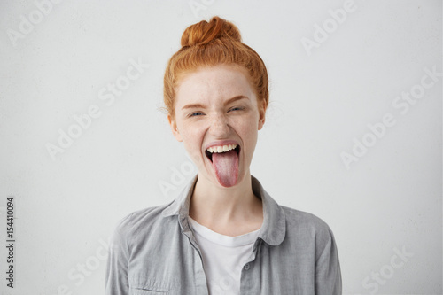 Canvas Print Naughty teenage girl with ginger hair and freckles misbehaving, sticking out her tongue at camera as a sign of disobedience, protest and disrespect