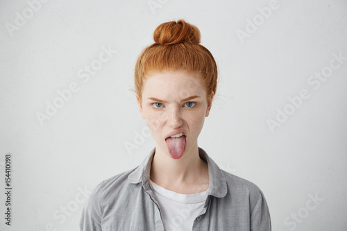 Headshot of naughty girl of European appearance sticking out tongue, trying to tease someone, looking immature and offensive, all her appearance expressing rudeness and disgust. Signs, symbols