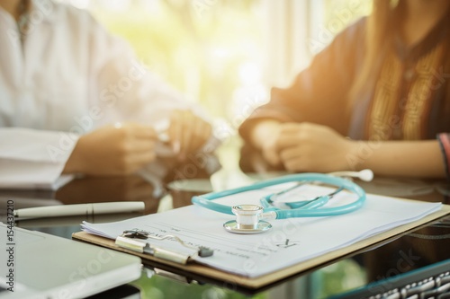 Stethoscope with clipboard and Laptop on desk,Doctor working in hospital writing a prescription, Healthcare and medical concept,test results in background,vintage color,selective focus photo