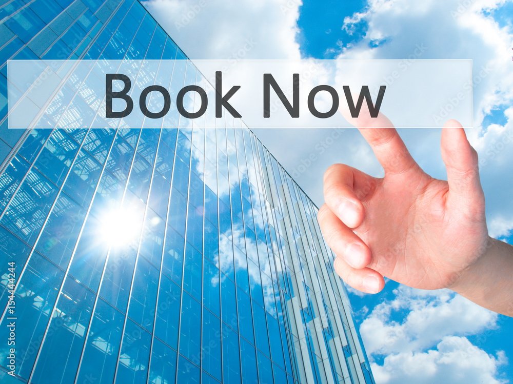 Book Now - Hand pressing a button on blurred background concept on visual screen. Book Now - Hand pressing a button on blurred background concept on visual screen.