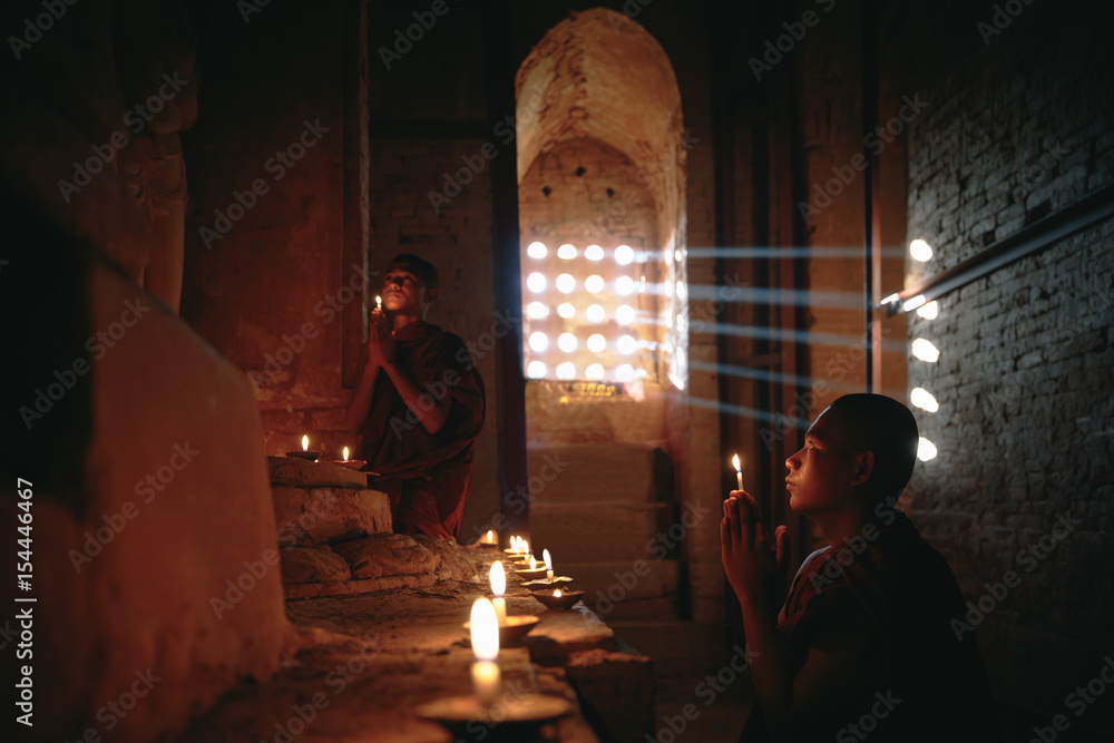 Novices praying with candles in front of buddha statue inside old pagoda, Bagan Myanmar