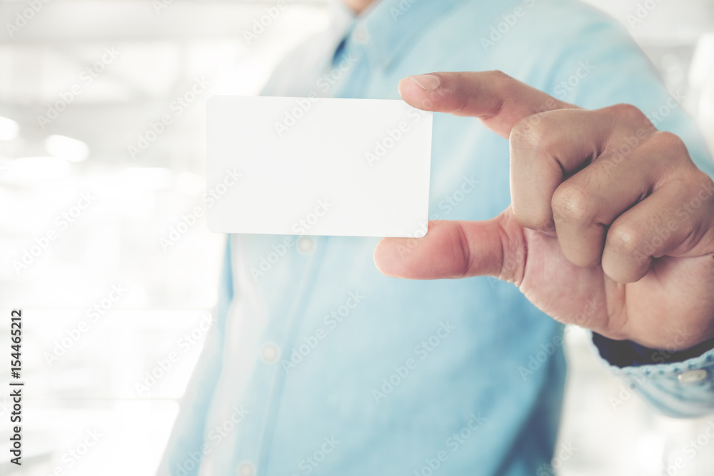 Young business man holding white business card on modern office blur background. Young business man holding white business card on modern office blur background.
