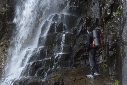 A backpacker with a backpack and the Mat is at a big waterfall among the rocks