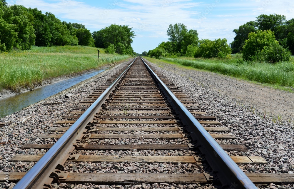 Railroad tracks on a green and rural summer countryside
