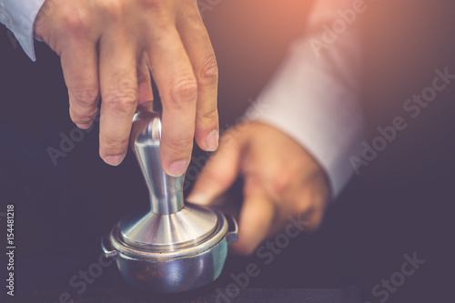 Hand of barista using tamper to press ground coffee into portafilter in cafe for prepare to make espresso coffee.