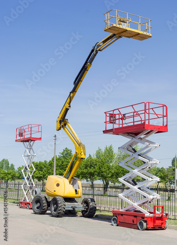 Two scissor and one articulated boom lift on asphalt ground