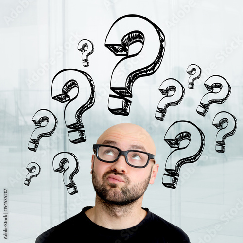 Portrait of an attractive stressed geek man with question mark icons surrounding his head - Problem concept