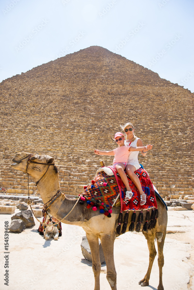 Fototapeta premium Tourists woman and girl are riding a camel in the background of the pyramids in Egypt