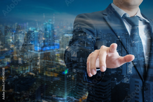 Double exposure of professional businessman touch digital screen with cityscape of business in Technology and business concept