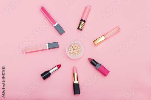 Lip gloss, lipstick and powder on a pink background.flat lay