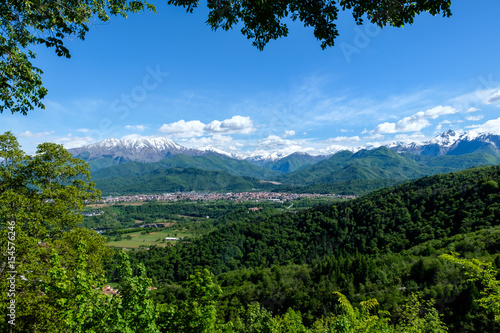South view of piedmontese alps with snowy mountains and woods in spring from the Sanctuary of Madonna degli Alpini, in Cervasca, Cuneo, Italy. The town of Borgo San Dalmazzo is also visible. photo