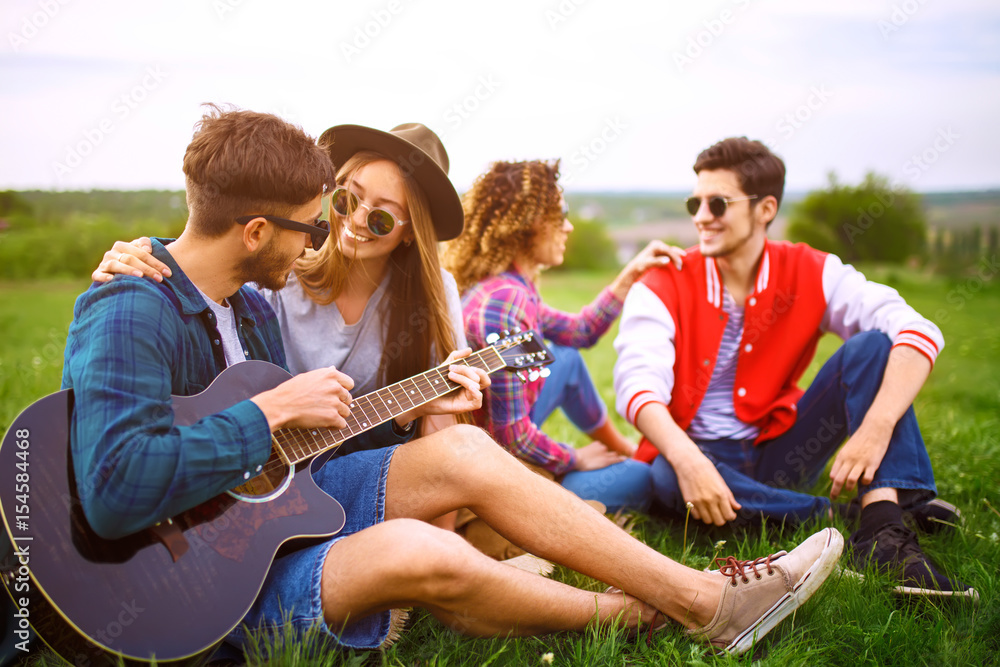 Group of friends enjoying party. The guy plays the guitar. Everyone has a great mood. Summer time. 

