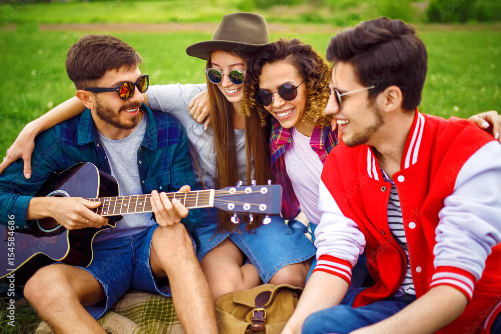 Group of friends enjoying party. The guy plays the guitar. Everyone has a great mood. Summer time. 

