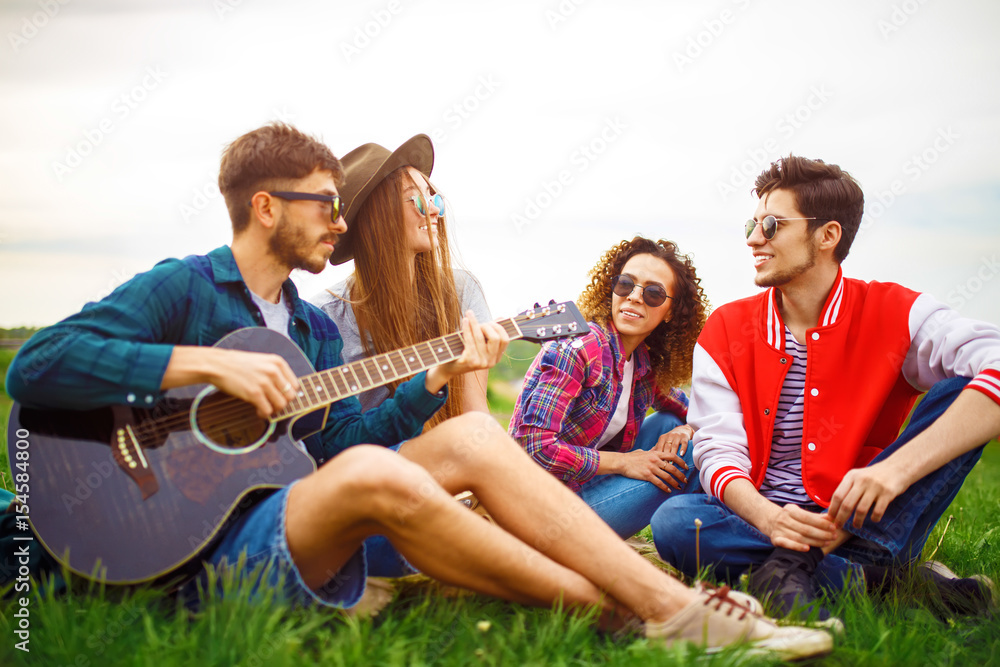 Group of friends enjoying party. The guy plays the guitar. Everyone has a great mood. Summer time. 

