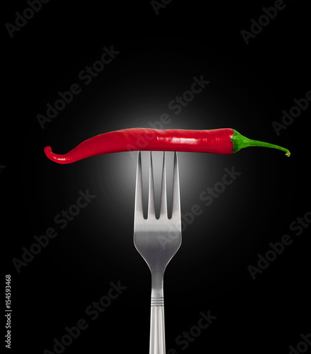 Red hot chili pepper speared onto metal fork shot on black backg