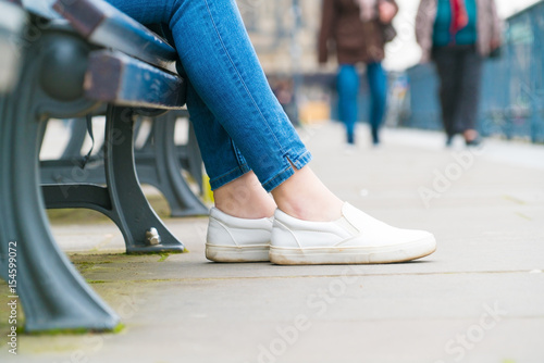 Legs of a girl sitting on a bench in the city