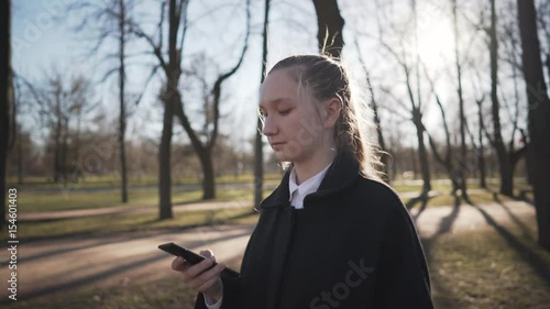 Gimbal shot of female teen girl using smartphone and walking on town alley in spring sunny day, uhd prores footage photo