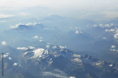 Sky scenery. Aerial view above the clouds and misty mountain peaks covered with snow on a sunny day. Swiss Alps.