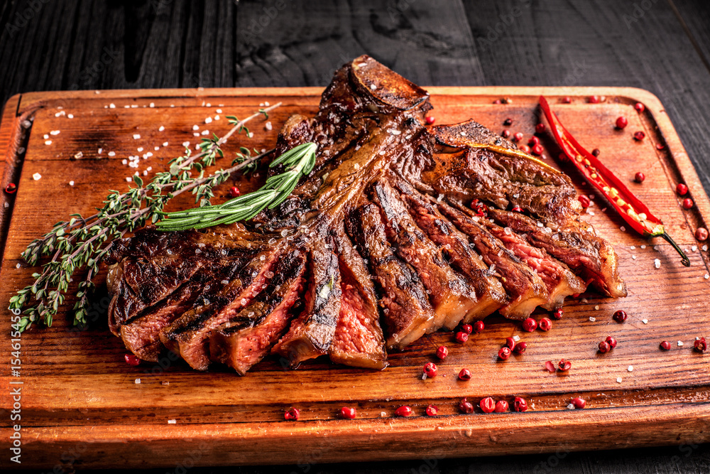 Sliced medium rare grilled steak on rustic cutting board with rosemary and spices , dark rustic wooden background, top view