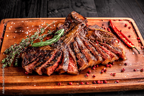 Sliced medium rare grilled steak on rustic cutting board with rosemary and spices , dark rustic wooden background, top view