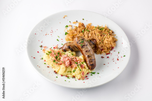 Grilled sausages, potatoes and braised cabbage on white plate close-up view from above.