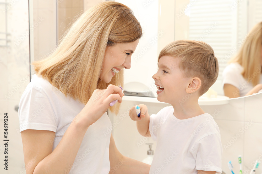 Beautiful mother and happy son brushing teeth near mirror in bathroom Beautiful mother and happy son brushing teeth near mirror in bathroom