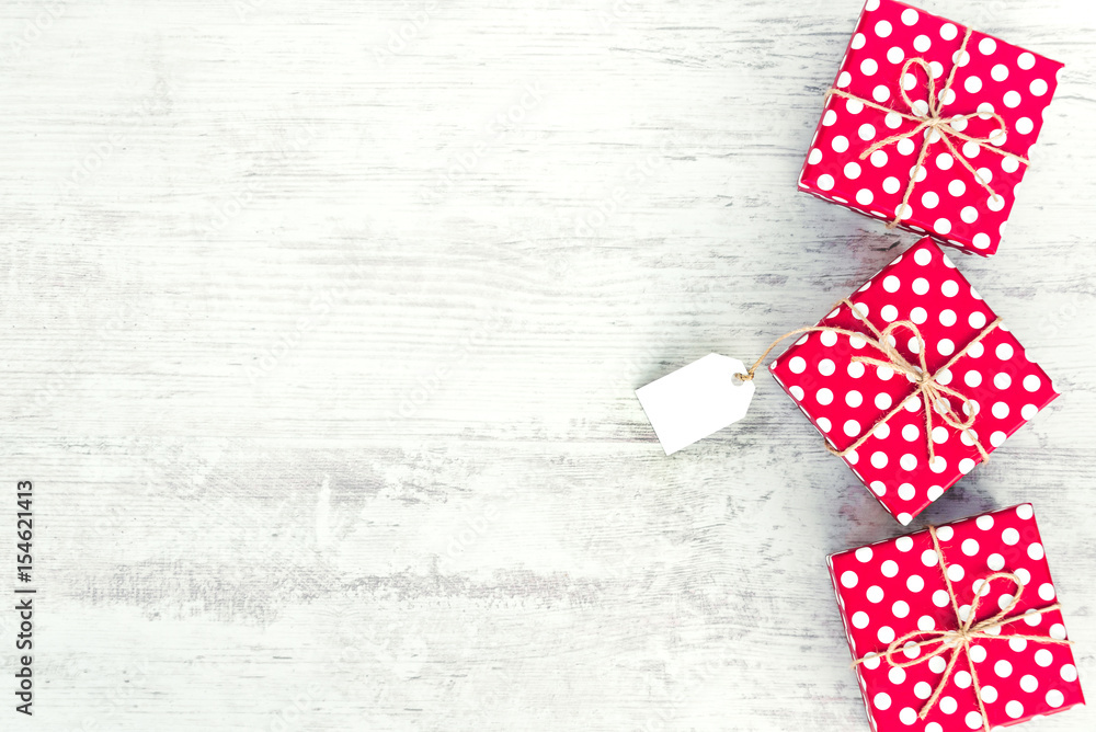 Empty card tied over red dotted gift box. Red dotted gift boxes over white wood background. Copy space. Empty card tied over red dotted gift box. Red dotted gift boxes over white wood background. Copy space.