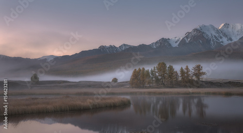 Misty autumn morning, a picturesque mountain lake on a background of snow capped mountains
