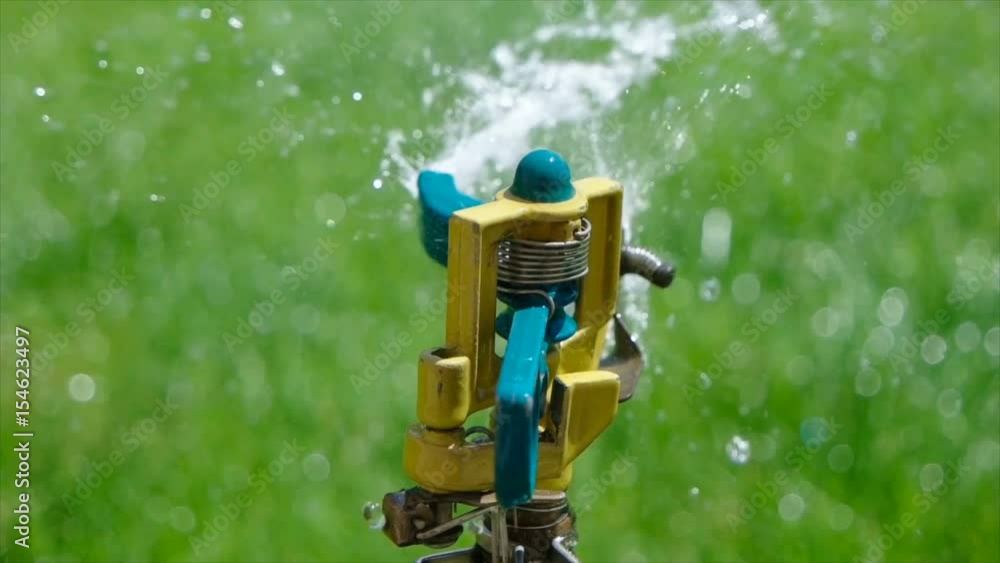 Watering the green grass by yard sprinkler. Sparkling water spraying