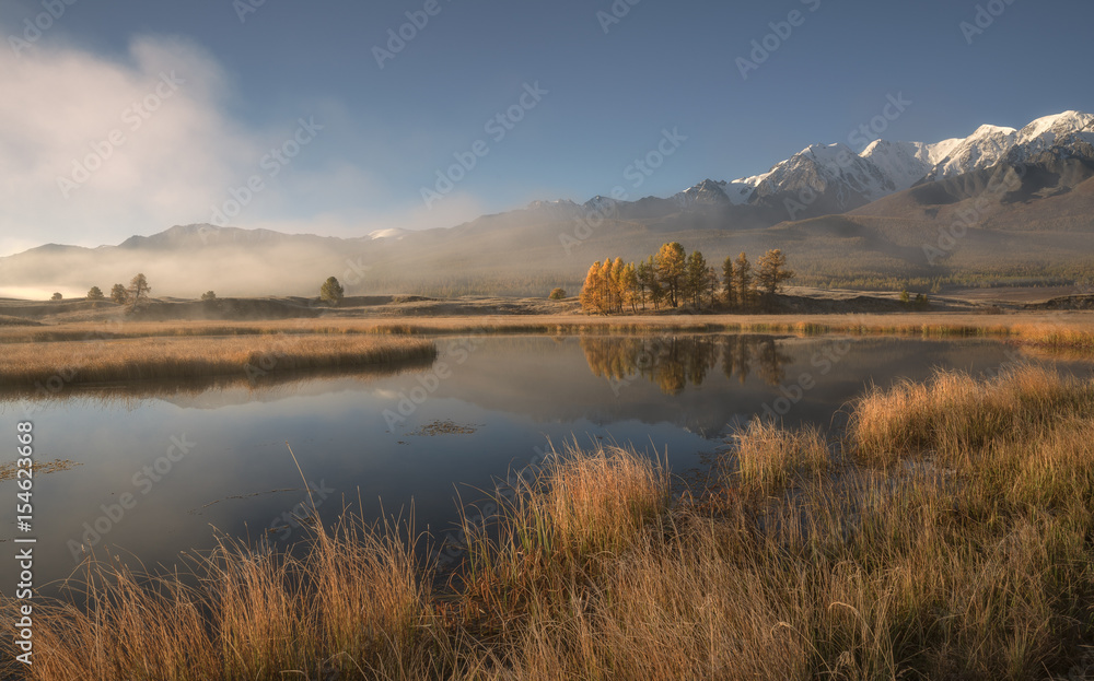 Mountain lake in the morning mist on the background of snowy mountains and blue sky