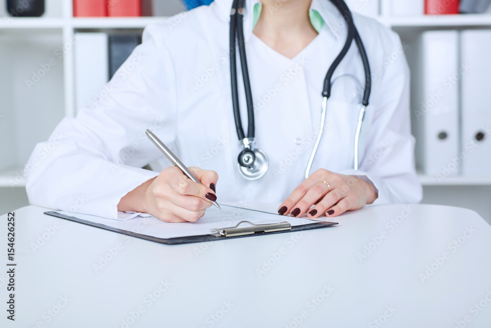 Female doctor filling out medical form while consulting patient Female doctor filling out medical form while consulting patient