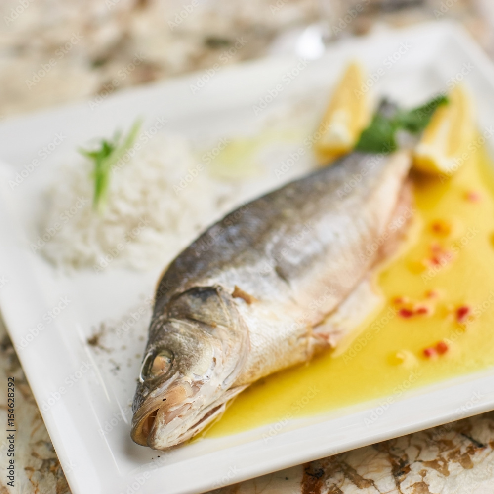 Whole boiled wolffish served with sauce from lemon butter and white wine on square white plate Whole boiled wolffish served with sauce from lemon butter and white wine on square white plate