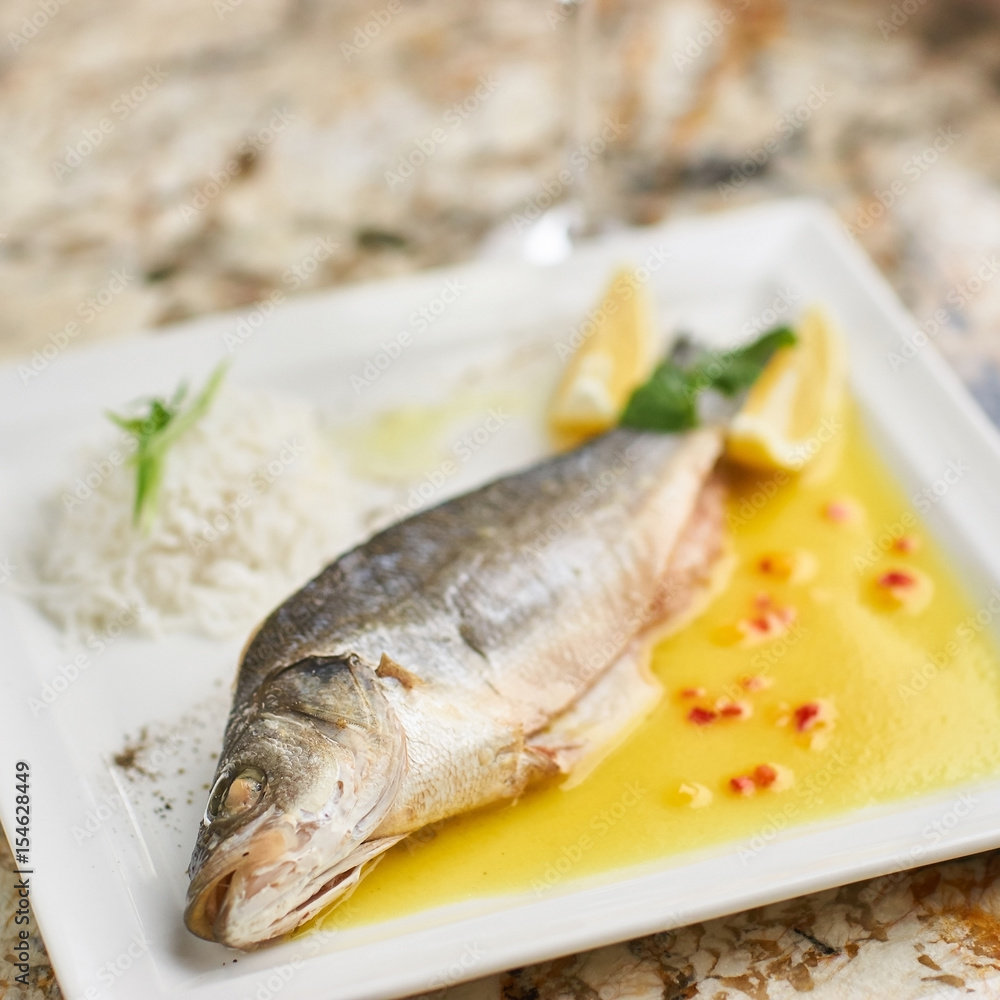 Whole boiled wolffish served with sauce from lemon butter and white wine on square white plate Whole boiled wolffish served with sauce from lemon butter and white wine on square white plate