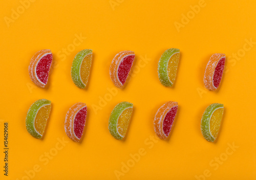 Still life of colored lobules of marmalade lying in two rows on an orange background