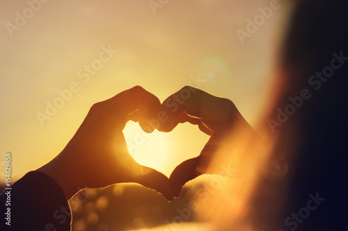 Young woman making heart with her hands at sunset