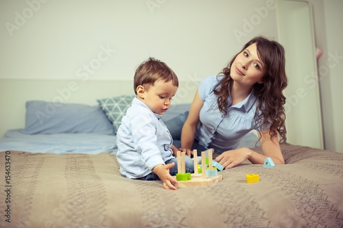 Young mom and young son sitting on the bed. Mom plays with her son. Family.