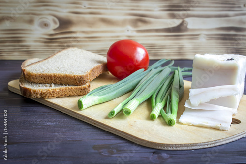 Lard (Salo), green onions, bread, red tomato on a wooden background.