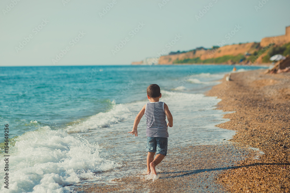 The boy running on a beautiful beach. The boy walking on a beautiful beach. Sea foam on the sand. lifestyle relationship contact pedigree ancestry